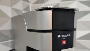 A coffee machine with a cup of coffee below it, set against a tiled wall.