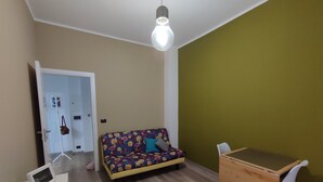A room with a sofa, a small wooden desk, and a light bulb hanging from the ceiling.
