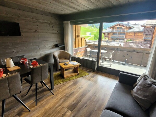 A modern interior with a dining area, sofa, and large windows offering a view of a ski resort.