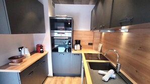 Une cuisine compacte équipée d’un four encastré, d’une machine à café et d’un évier avec un porte-serviette.