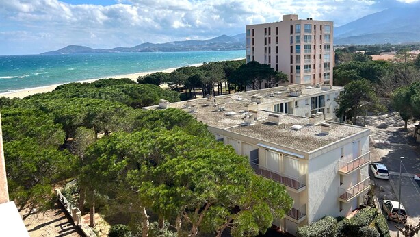 Ein Hochhaus mit Dachterrasse, umgeben von Bäumen und Blick auf den Strand.