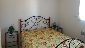 Een enkel bed met een bloemenprint deken, een metalen hoofdbord en twee nachtkastjes met lampen.