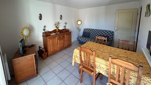 Een kamer met een eettafel, stoelen, een bank, een houten kast en een deur.
