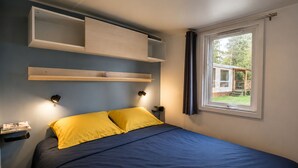 A bedroom with a bed, built-in shelving, bedside lamps, and a window with a view.
