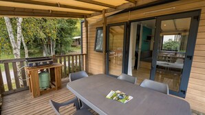 A covered outdoor area with a table and chairs, a grill, and a view of the surrounding greenery. - Mobile home 32m² with terrace, 3 bedrooms for 6 people (Granges-Aumontzey-Aumontzey)