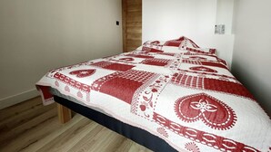 Ein Schlafzimmer mit einem Bett, das mit einer gemusterten Steude bezogen ist, einer Holztür und einer weißen Wand.