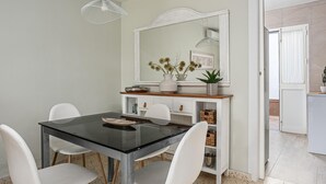 A dining area with a glass table, white chairs, a white console table with decorative items, and a large mirror above the console table.
