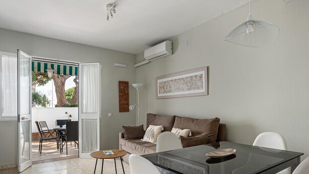 A modern living room with a glass dining table, white chairs, a brown sofa, and a ceiling fan.