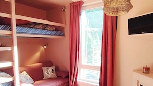 A cozy room with a bunk bed, a sofa, a wooden table, and a window with curtains. - Modern and cozy studio at the foot of the slopes in Isola 2000 (Isola 2000)
