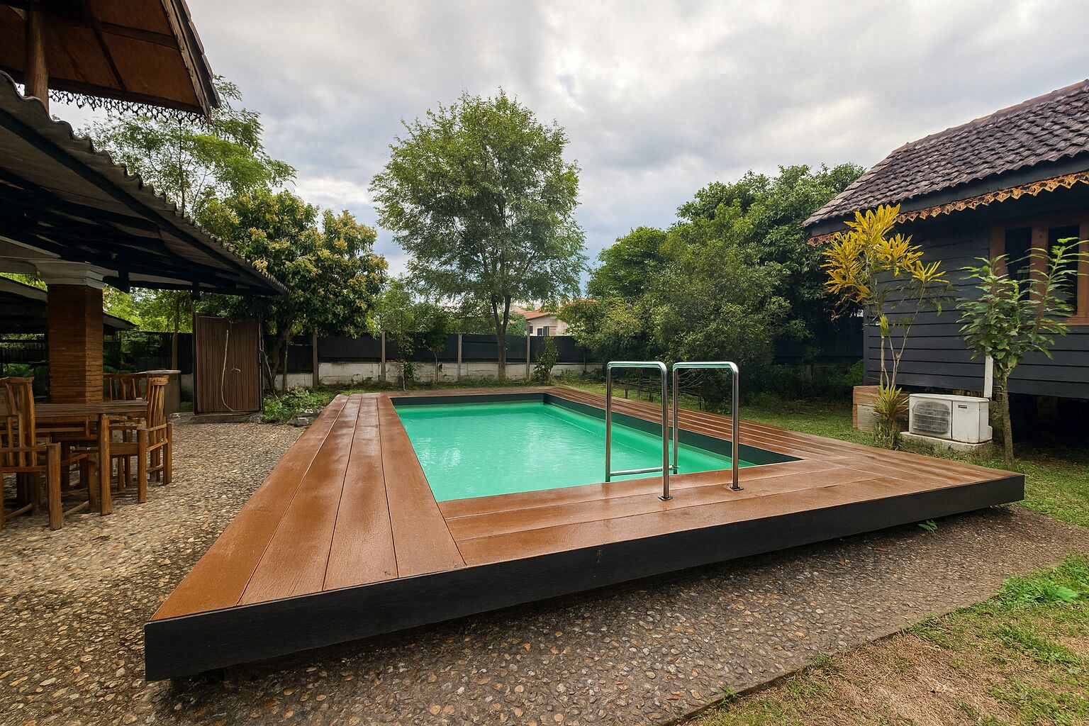 Una piscina rettangolare con un pontile in legno e ringhiere metalliche, circondata da alberi e una zona patio coperta.