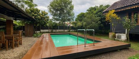 Una piscina rettangolare con un pontile in legno e ringhiere metalliche, circondata da alberi e una zona patio coperta.