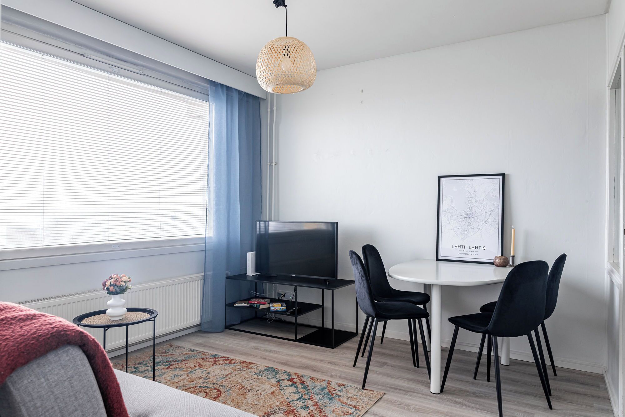 Moderni olohuone, jossa on televisio, ruokapöytä tuoleineen, kehystetty kartta ja pieni sivupöytä, jossa on maljakko.