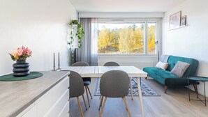 A modern living room with a dining area, a green sofa, a small table, and a view of autumn trees through large windows. - 1BR Apartments next to Railway Station, Free Parking, Balcony (Lahti)