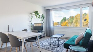 A modern living room with a dining area, a TV, and a view of autumn trees. - 1BR Apartments next to Railway Station, Free Parking, Balcony (Lahti)