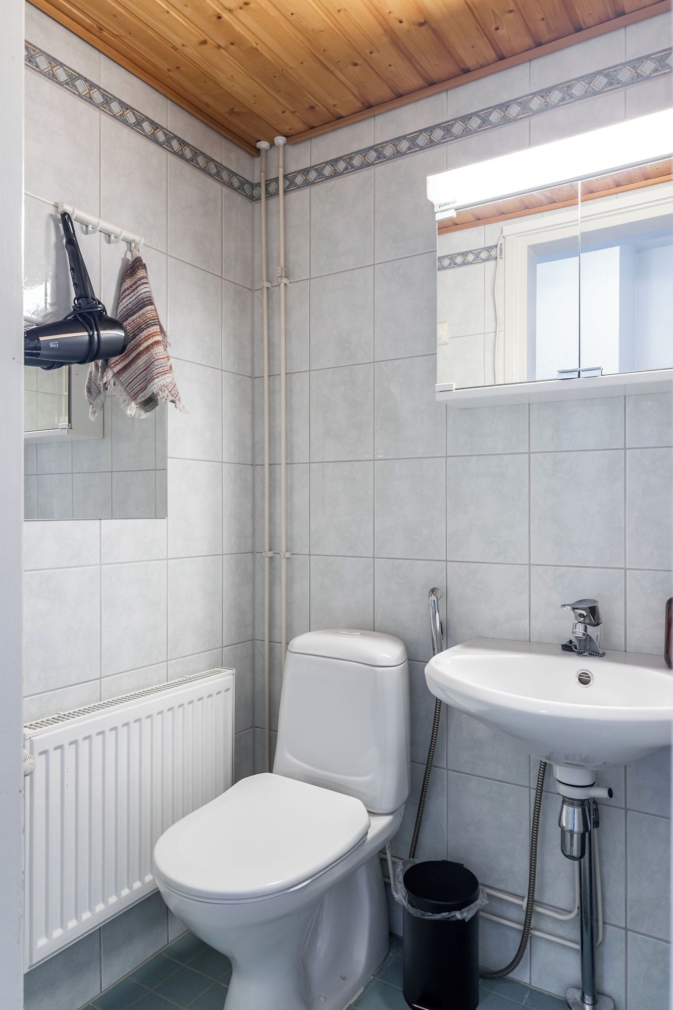 A bathroom with a white toilet, a white sink, and a shower. There is a towel hanging on a rack and a black trash bin.