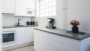 A modern kitchen with white cabinets, a built-in oven, a coffee machine, and a vase with flowers on the counter. - 1BR Apartments next to Railway Station, Free Parking, Balcony (Lahti)