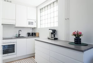 Una cocina moderna con armarios blancos, horno empotrado, cafetera y un florero con flores en la encimera.