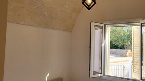 Une chambre à coucher avec un lit, une table de chevet, une lampe et une fenêtre dont le volet est ouvert.
