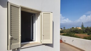 Un balcon avec un mur blanc et une fenêtre dont les volets sont ouverts.