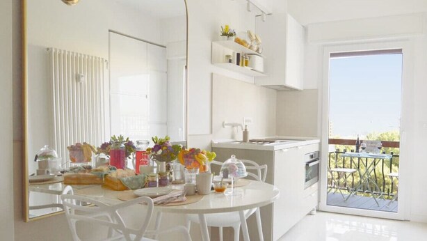A modern kitchen with white cabinets, a dining area with white chairs, and a view of the outdoors through a sliding glass door. - TraStella: Classy Rome Stay close to Trastevere St, (Roma)