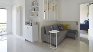 A modern living room with a sofa, a small white table, and a white cabinet. There is a radiator, a coffee machine, and a shelf with framed pictures. - TraStella: Classy Rome Stay close to Trastevere St, (Roma)