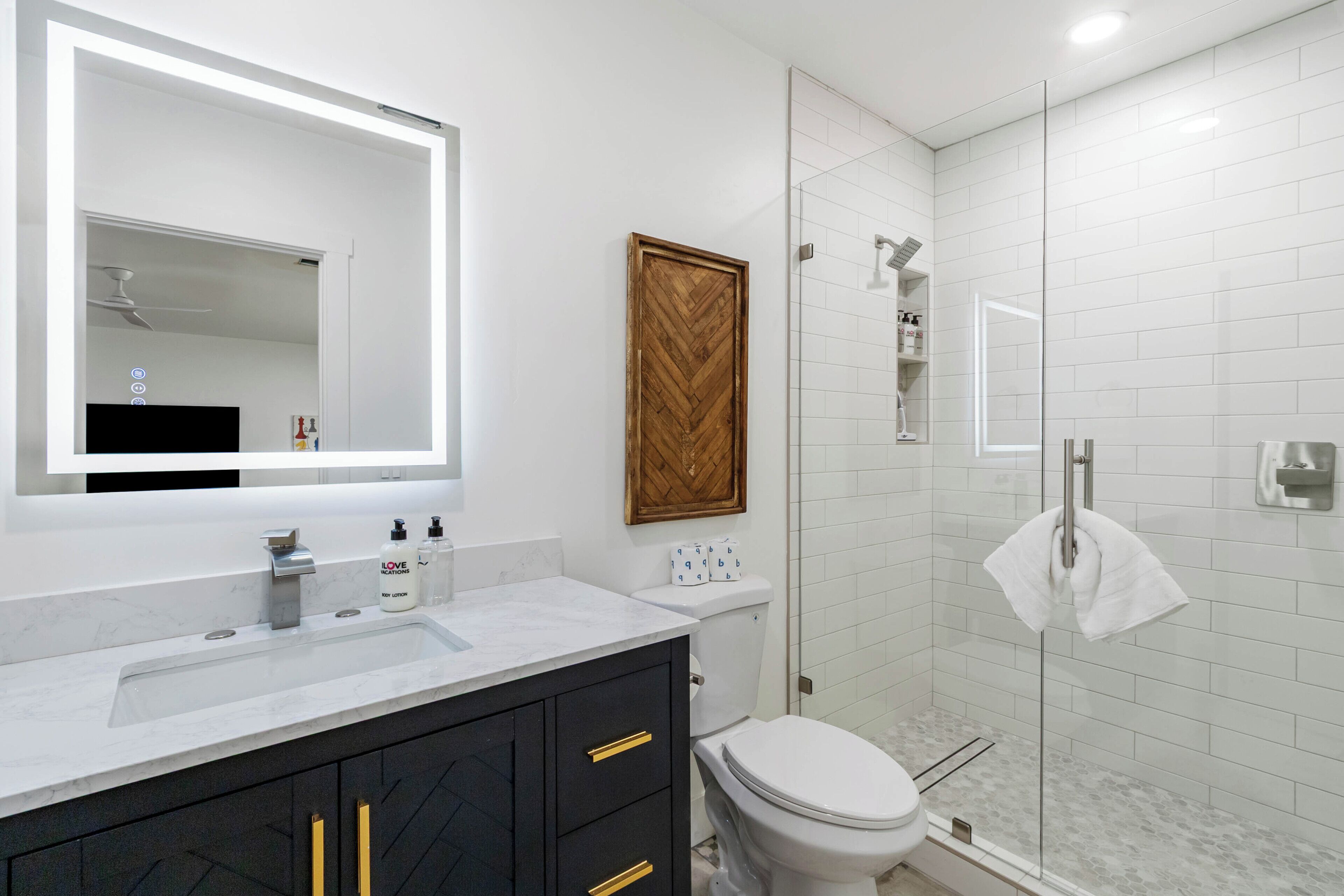 A modern bathroom with a white vanity, a large mirror, a wooden door, and a glass shower enclosure.