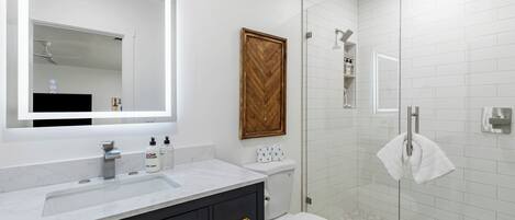 A modern bathroom with a white vanity, a large mirror, a wooden door, and a glass shower enclosure.