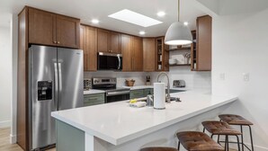 Een moderne keuken met een roestvrijstalen koelkast, een magnetron en een groot kookeiland met barstoelen.