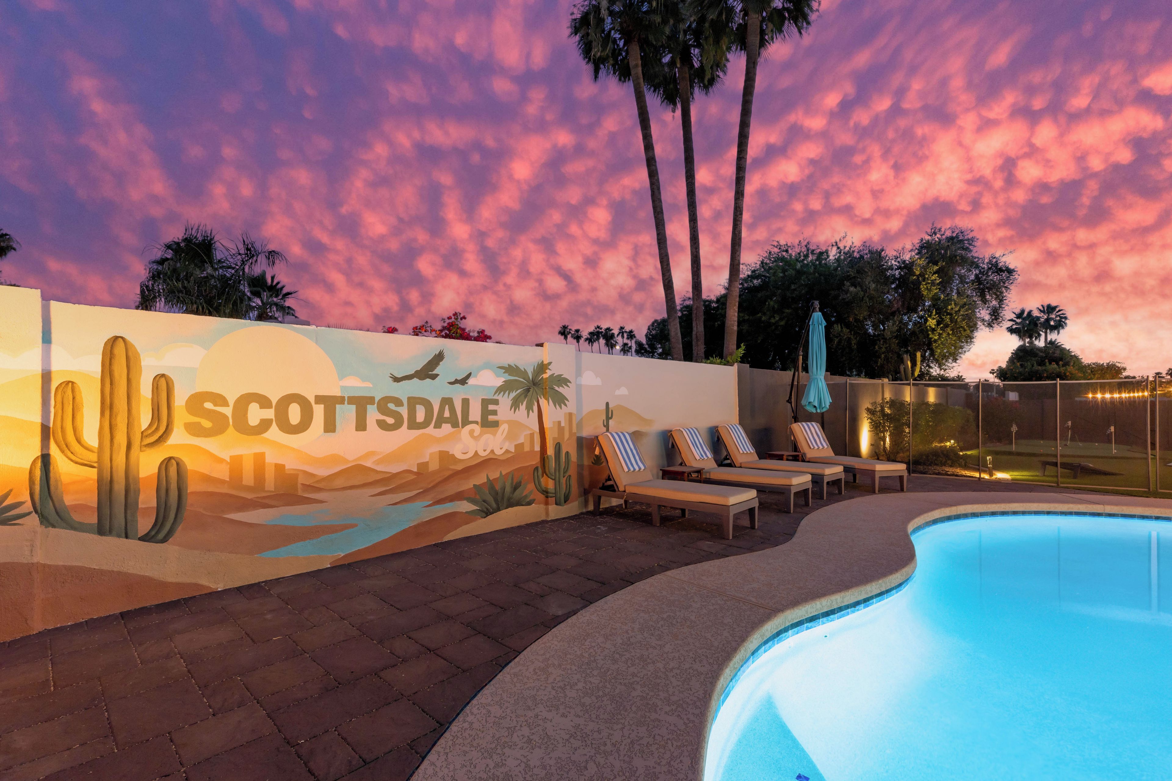 A pool area with lounge chairs and a mural of a desert landscape.