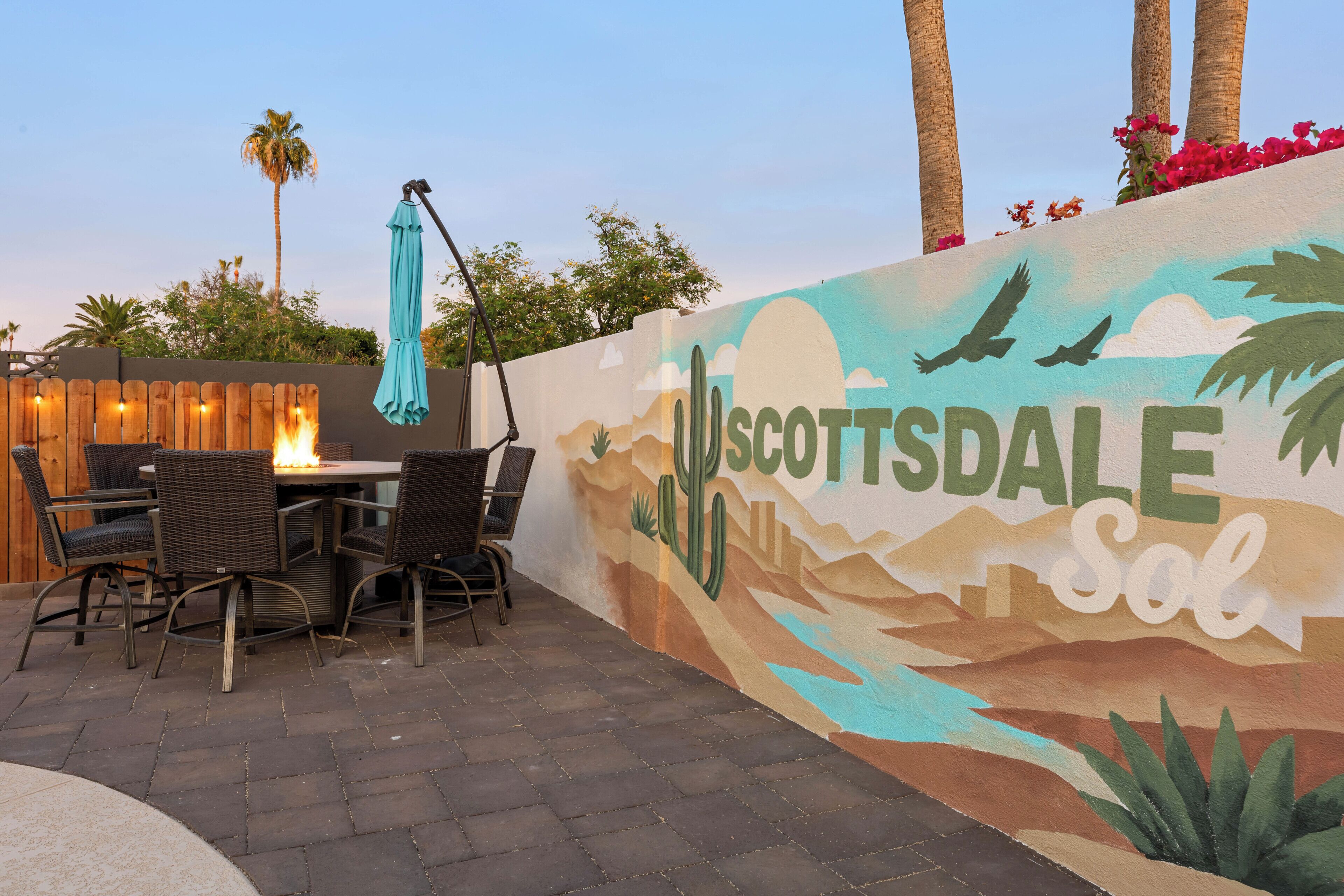 A patio area with a mural of Scottsdale, Arizona, a table with chairs, and a hanging umbrella.