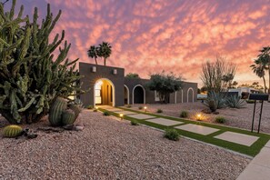 A desert-style building with arched doorways, a gravel pathway, and cacti.