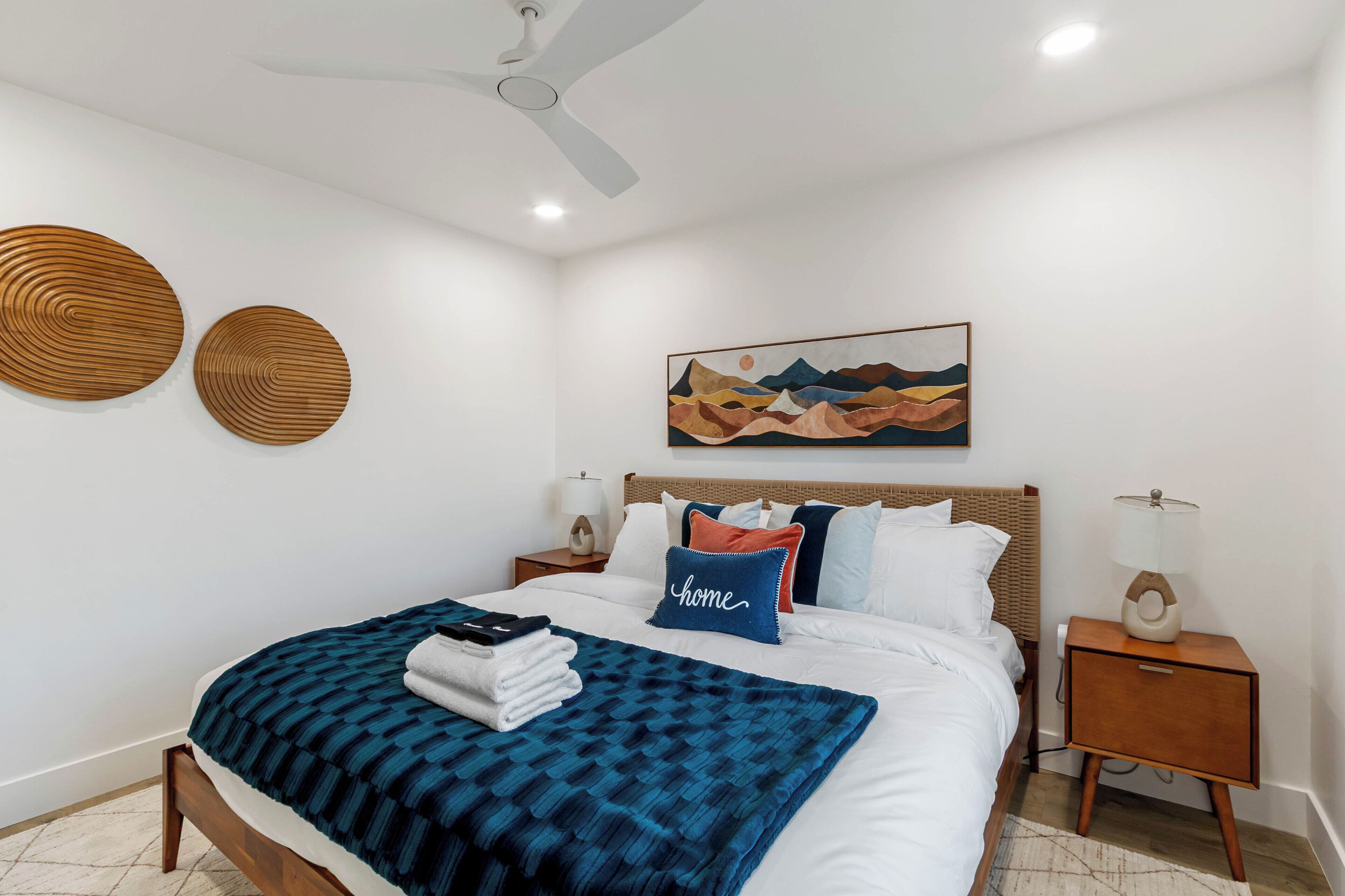 A neatly arranged bedroom with a bed, bedside tables, a ceiling fan, and a wall-mounted artwork.