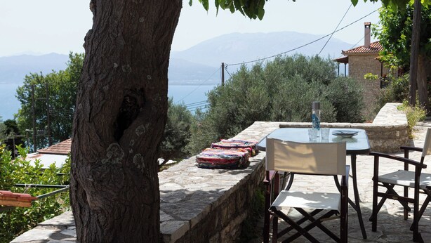 A stone table and chairs set on a terrace overlooking a body of water and mountains. - To spiti sto castro (Nafpaktos)