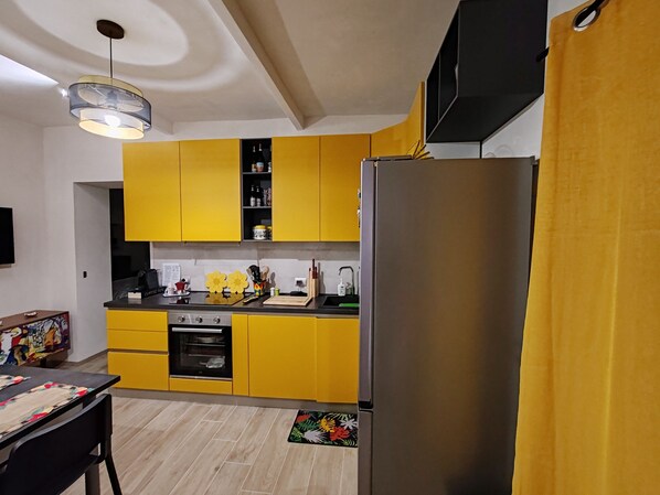 A modern kitchen with yellow cabinets, a stainless steel refrigerator, and a black countertop.