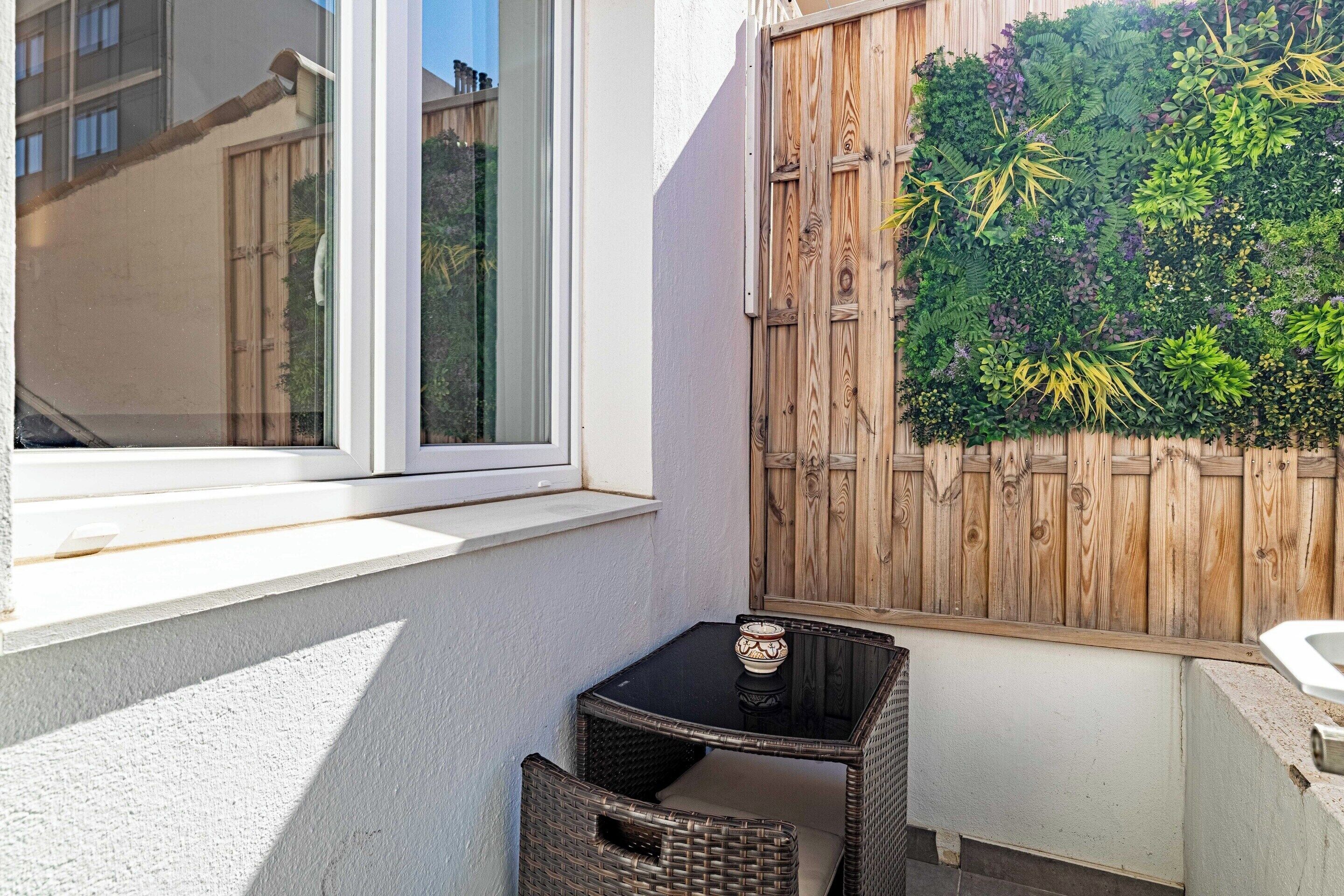 Ein kleiner Außenbereich mit Tisch und Stühlen, ein Fenster und ein Holzzaun mit vertikalem Garten.