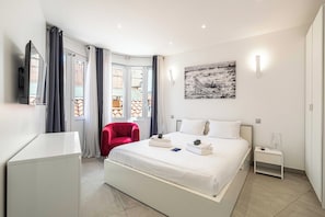 A hotel room with a large bed, a red chair, a desk, a nightstand, and a painting on the wall. - Cozy apt in the Heart of Cannes- Croisette/beaches (Cannes)