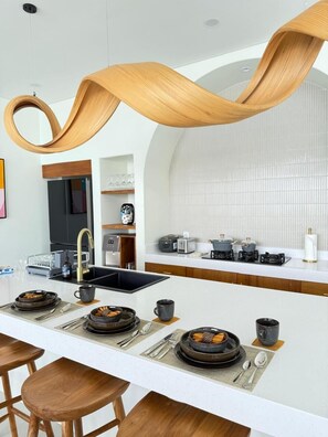 A modern kitchen with a central island, wooden stools, and a sleek backsplash. - Marcio Luxury Villa by Bali Lyfe Venture (Jimbaran)