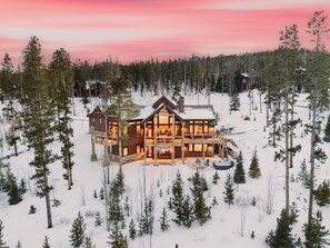 A large, multi-story lodge with a prominent central deck and multiple rooms, surrounded by a snowy forest. - Brighton House | Highlands Luxury Mountain Escape (Breckenridge)