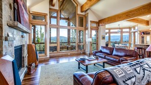 A spacious living room with a fireplace, leather sofas, and large windows offering mountain views.