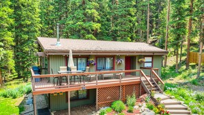 A two-story cabin with a deck, outdoor seating, and a staircase leading to a covered porch.