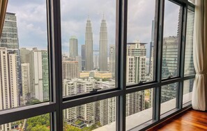 A high-rise hotel room with large windows offering a view of the cityscape, including the Petronas Twin Towers.