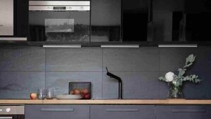 Une cuisine moderne avec des meubles de couleur sombre, un four en acier inoxydable et un coin repas comprenant une table ronde et un canapé blanc.