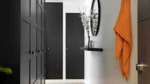 Un couloir avec un plancher en bois, une armoire noire, un miroir et un vase avec des fleurs posé sur une étagère.