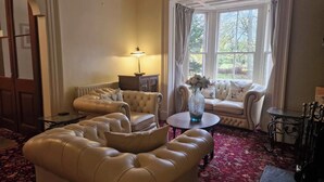 A cozy living room with a large window, a sofa, a loveseat, a coffee table, and a lamp. - Lovelady Shield House (Alston)