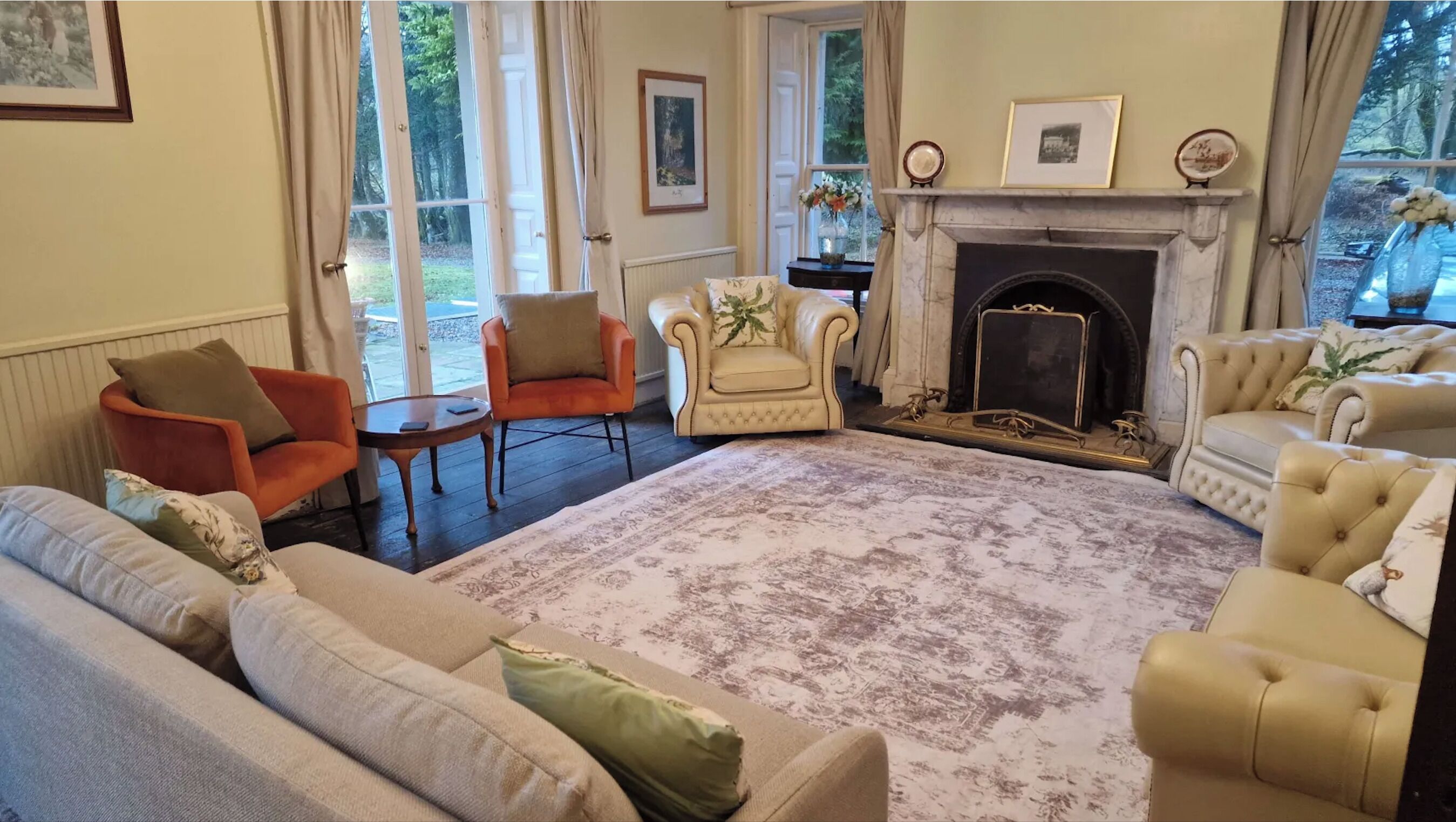 A living room with a fireplace, two armchairs, a sofa, and a large rug.