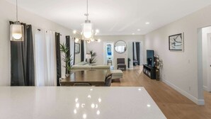 A modern living room with a large dining table, a sofa, and a TV. There is a chandelier hanging from the ceiling and a plant on the side. - Pet Friendly, Modern, Mins to Retro Row & Beach (Long Beach)