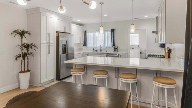 A modern kitchen with white cabinets, a central island with stools, a stainless steel refrigerator, and pendant lighting. - Pet Friendly, Modern, Mins to Retro Row & Beach (Long Beach)