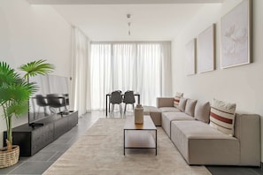 Uma sala de estar moderna com sofá, televisão e um espaço de jantar com cadeiras.