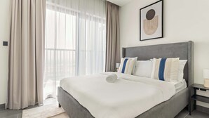 A modern hotel room with a large bed, a bedside table, and a window with sheer curtains.