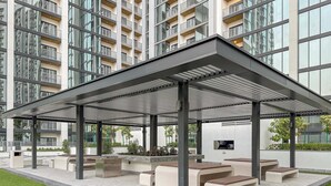 A covered outdoor seating area with benches and planters, surrounded by a modern building with balconies.